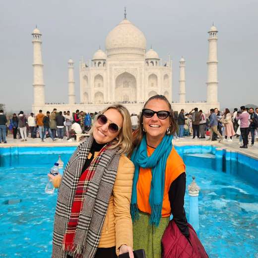 Dos amigas con bufandas sonriendo frente al Taj Mahal, India